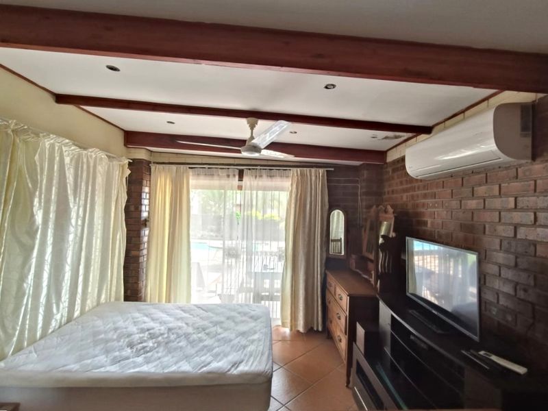 Bedroom featuring exposed brick walls, timber ceiling beams, tiled flooring, and a split-system air conditioner with direct access to the outdoor area.