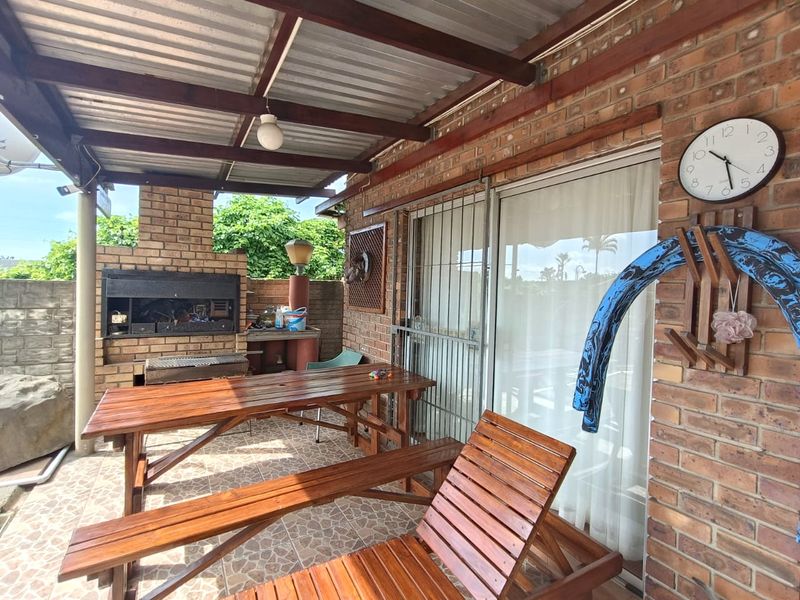 Covered outdoor patio featuring a built-in brick braai, tiled flooring, and direct access to the interior through a sliding glass door.