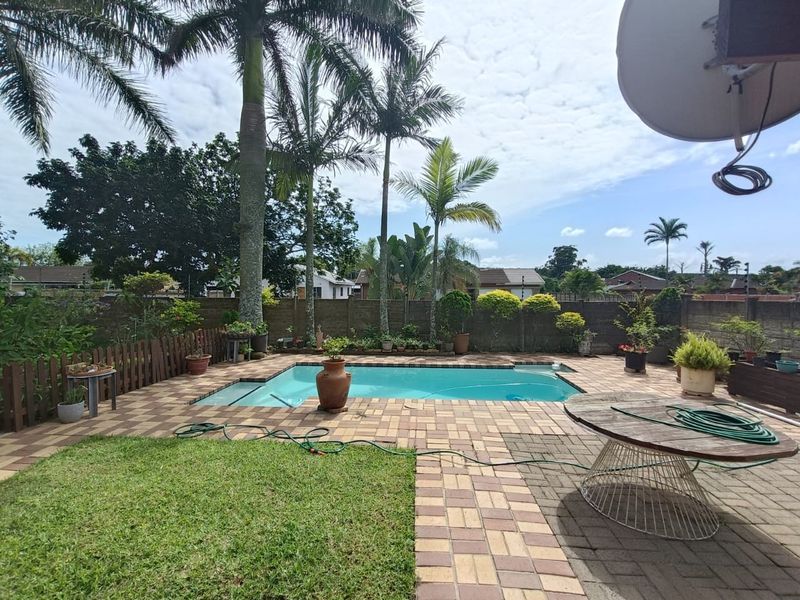 A private outdoor pool area featuring a paved deck, established palm trees, and a secure boundary wall, perfect for relaxation and outdoor entertaining.