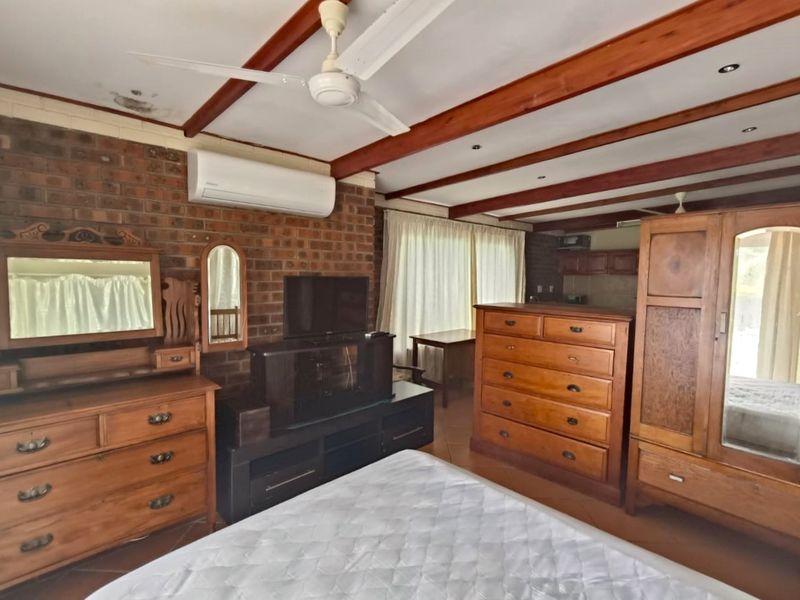 Spacious bedroom featuring exposed brick walls, timber ceiling beams, tiled flooring, and a split-system air conditioner for climate control.