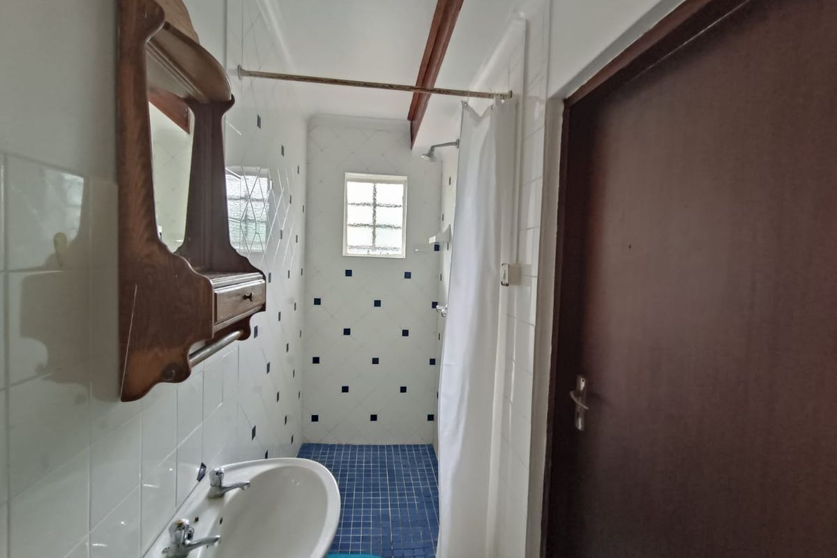 A compact bathroom featuring a pedestal basin, shower area with curtain, and blue tiled flooring with matching wall accents.