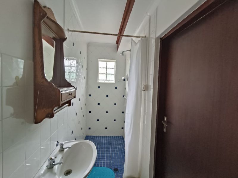 A compact bathroom featuring a pedestal basin, shower area with curtain, and blue tiled flooring with matching wall accents.