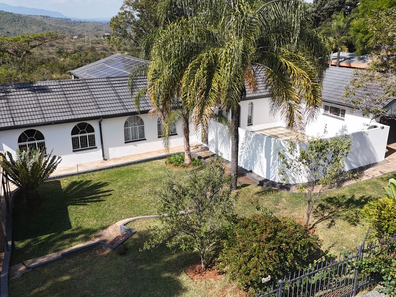 Aerial view of a well-maintained residential property featuring a tiled roof with solar panels, arched windows, and a spacious landscaped garden.