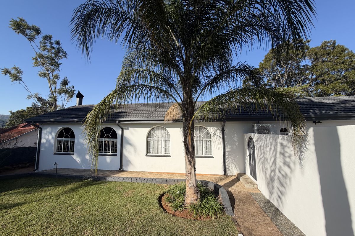 Rear view of the property featuring a well-maintained lawn, mature palm tree, paved walkway, and white exterior walls with arched windows.