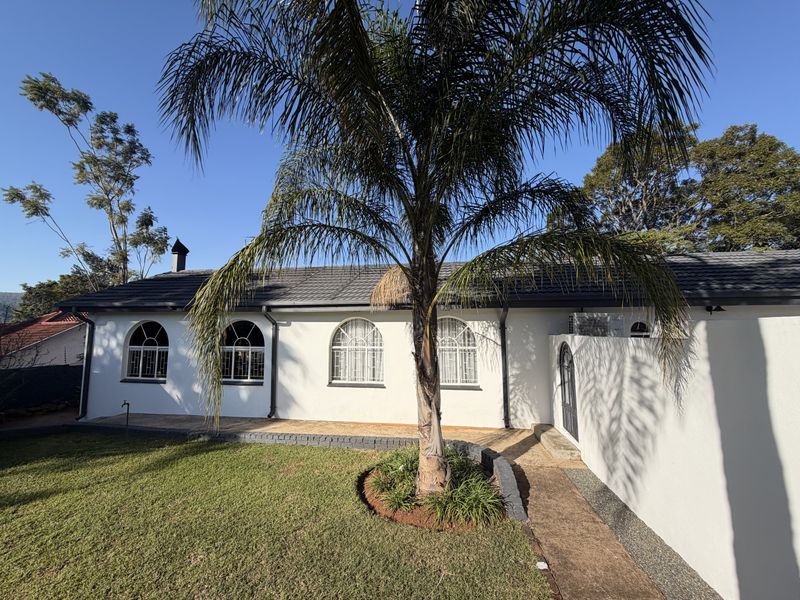 Rear view of the property featuring a well-maintained lawn, mature palm tree, paved walkway, and white exterior walls with arched windows.