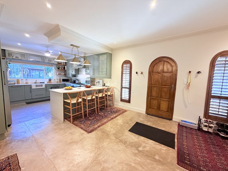 Spacious open-plan kitchen and entry area featuring a large island, custom cabinetry, farmhouse sink, and elegant arch-top wooden door with polished concrete floors.
