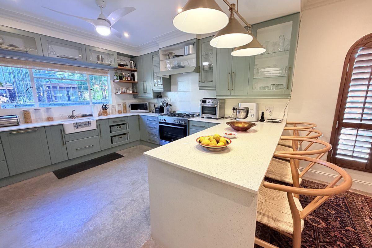 Modern kitchen featuring sage green shaker-style cabinetry, quartz countertops, a farmhouse sink, and a central island with breakfast bar seating.