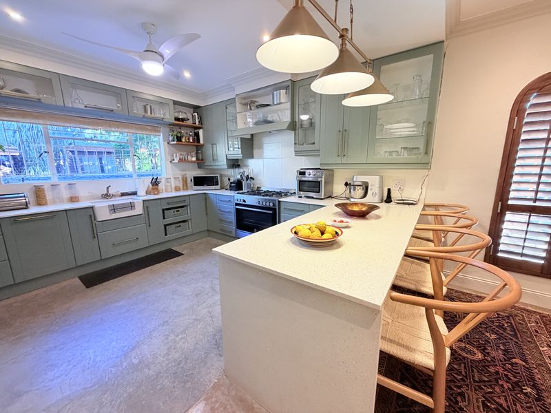 Modern kitchen featuring sage green shaker-style cabinetry, quartz countertops, a farmhouse sink, and a central island with breakfast bar seating.