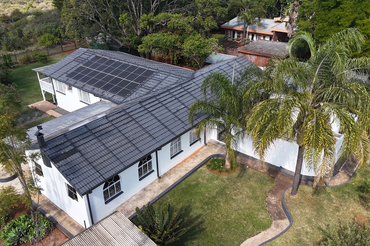 Aerial view of the property featuring a well-maintained tiled roof with integrated solar panels, surrounded by a landscaped garden and paved pathways.