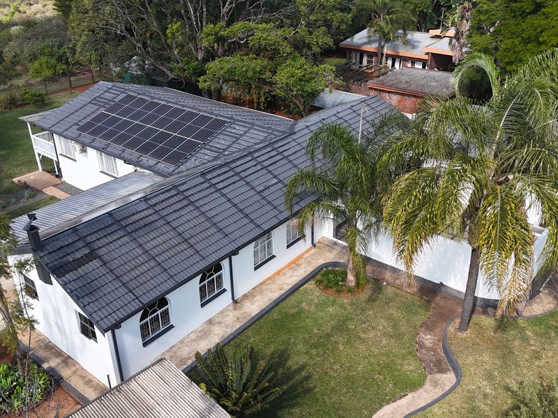 Aerial view of the property featuring a well-maintained tiled roof with integrated solar panels, surrounded by a landscaped garden and paved pathways.