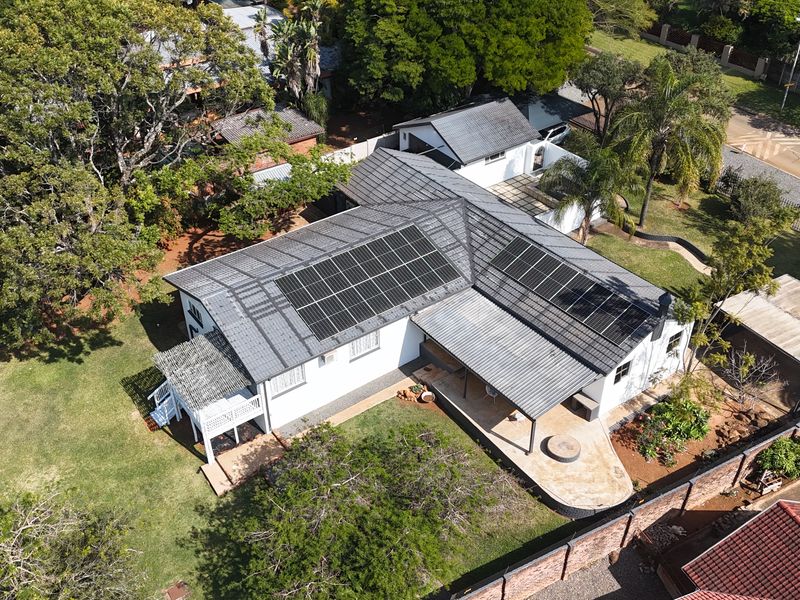 Aerial view of a residential property featuring a tiled roof with installed solar panels, a covered patio area, and a spacious garden.