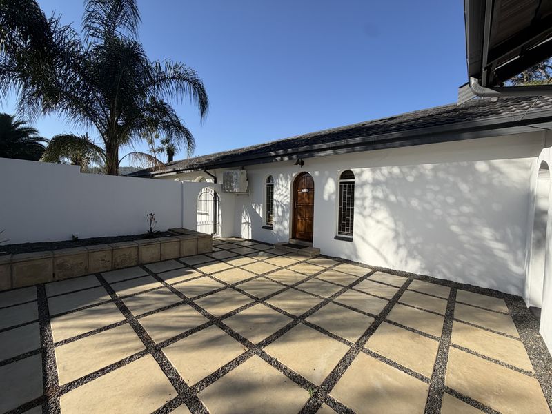 A well-maintained rear patio area featuring paved flooring, a retaining wall, and secure access to the home through an arched wooden door.