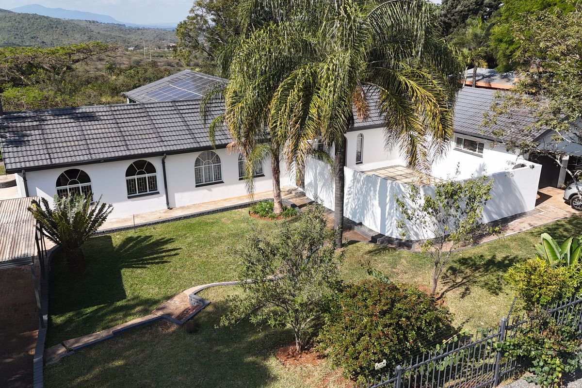Aerial view of a well-maintained residential property featuring a tiled roof with solar panels, arched windows, and a spacious landscaped garden.
