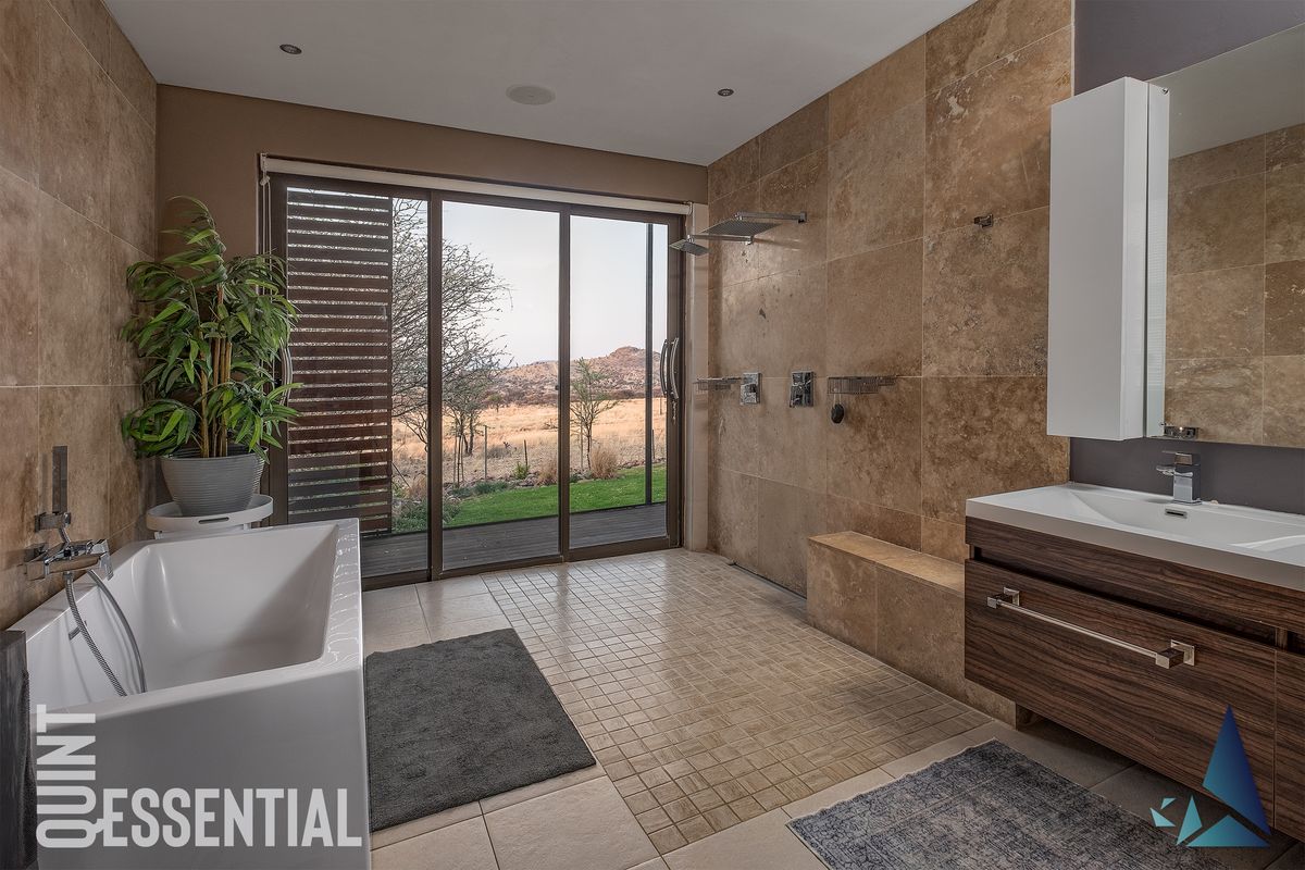Modern bathroom featuring a freestanding bathtub, walk-in shower with stone tiling, floating vanity, and large sliding glass doors opening to a scenic outdoor view.