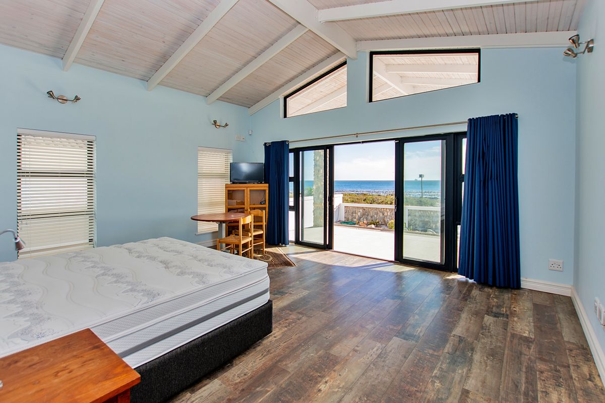 Spacious bedroom featuring vaulted ceilings with exposed rafters, laminate flooring, and large sliding glass doors opening to a scenic coastal view.