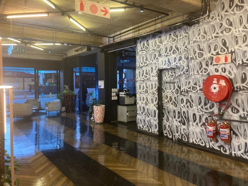 A modern industrial-style lobby or clubhouse area featuring exposed concrete ceilings, track lighting, and distinctive herringbone timber flooring with graffiti-style wall art.