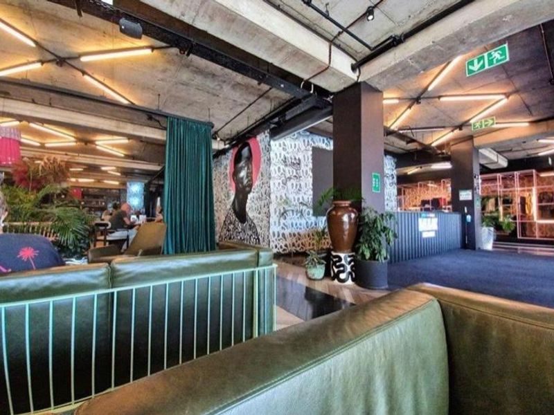 A modern open-plan living area featuring an industrial aesthetic with exposed concrete ceilings, track lighting, and structural columns.