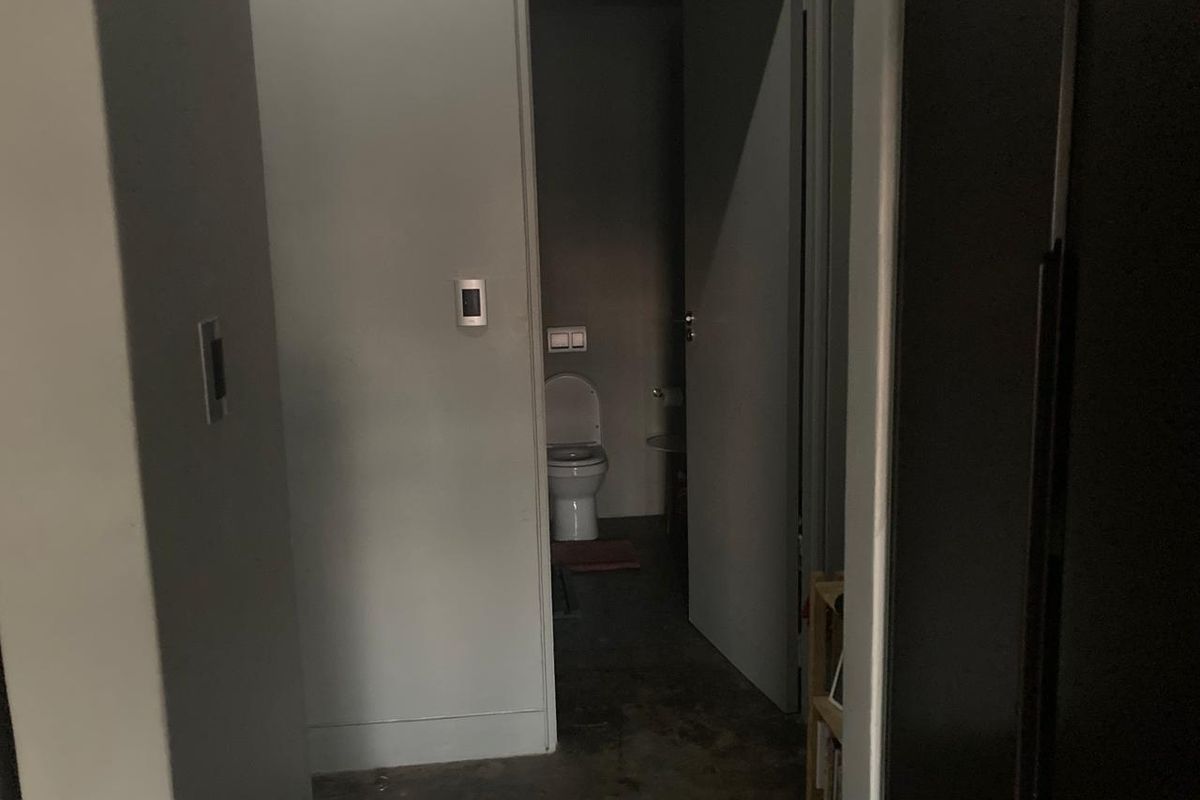 A dimly lit, sparse bathroom featuring a standard toilet and wall-mounted fixtures, requiring improved lighting and cosmetic updates.