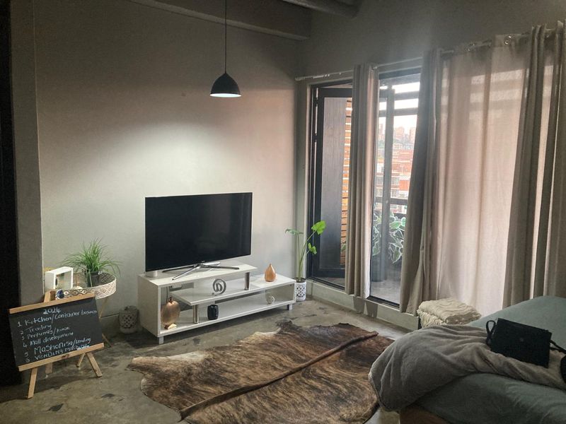 A modern living room featuring polished concrete floors, industrial-style pendant lighting, and large sliding glass doors leading to a balcony.
