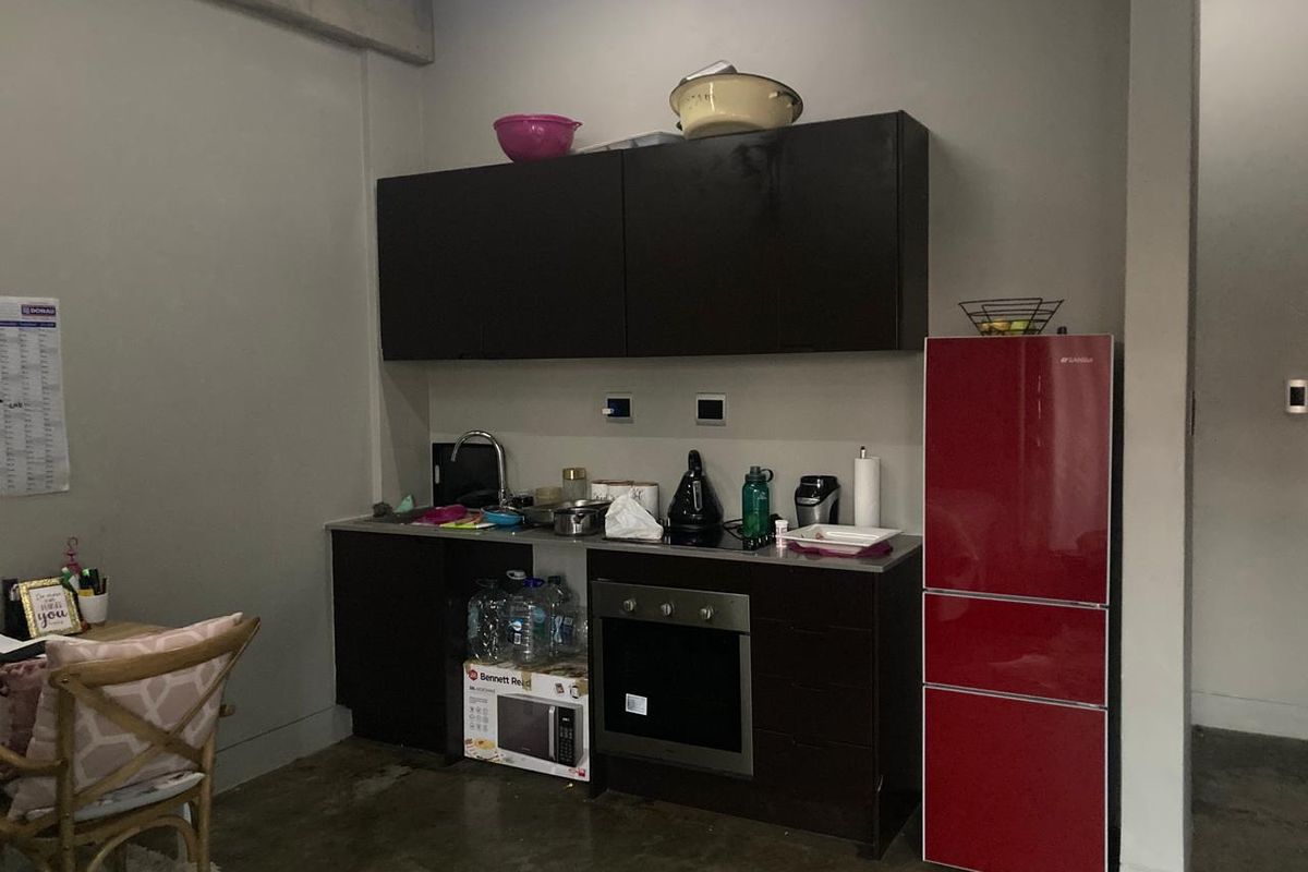 Compact kitchen area featuring dark cabinetry, stainless steel sink, built-in oven, and cooktop, set against a neutral wall with concrete flooring.