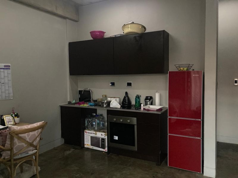 Compact kitchen area featuring dark cabinetry, stainless steel sink, built-in oven, and cooktop, set against a neutral wall with concrete flooring.