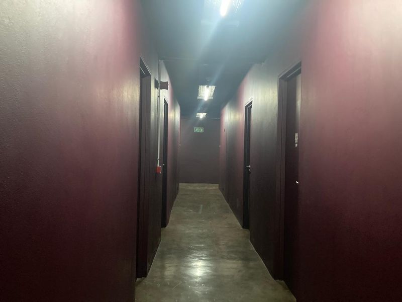 A dimly lit apartment hallway featuring dark painted walls, concrete flooring, and multiple access doors.