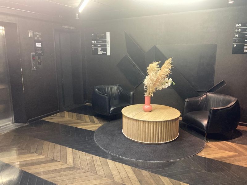A modern apartment building lobby featuring dark walls, herringbone wood flooring, and elevator access.