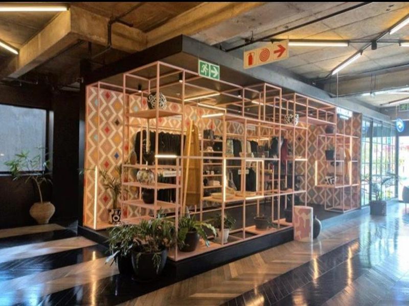 A modern commercial or retail space featuring an industrial aesthetic with exposed concrete ceilings, herringbone flooring, and a prominent geometric metal display structure.