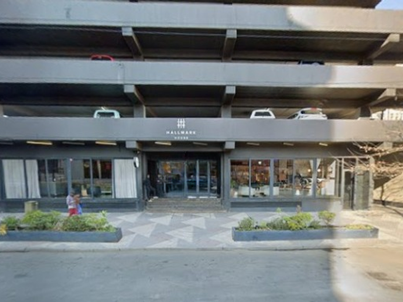 Front elevation of Hallmark House apartment building featuring a multi-level parking structure, glass entrance, and paved forecourt with built-in planters.
