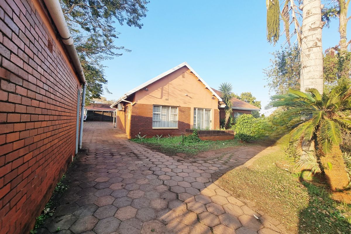 A view of the side and rear exterior of the house, featuring a paved driveway, brick facade, and established garden area.