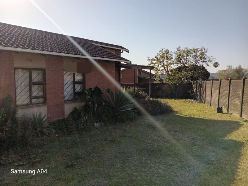 A view of the rear exterior of the house featuring a brick facade, tiled roof, and a spacious backyard with perimeter walling.