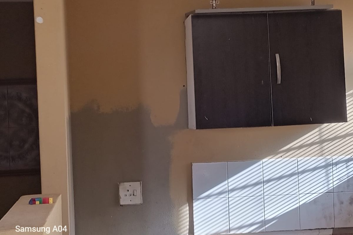A kitchen area featuring wall-mounted cabinetry and tiled splashback, currently showing signs of incomplete maintenance and wear.