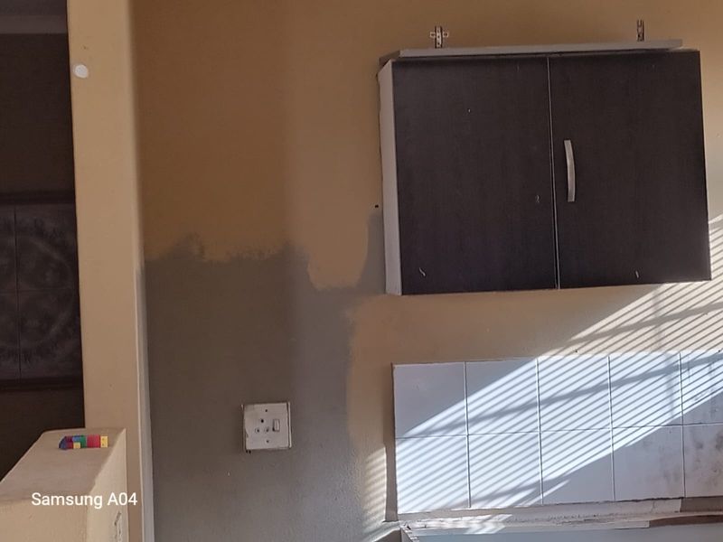 A kitchen area featuring wall-mounted cabinetry and tiled splashback, currently showing signs of incomplete maintenance and wear.