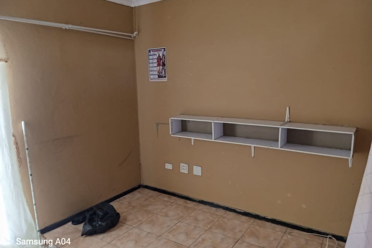 A small, empty room featuring tiled flooring, a wall-mounted storage shelf, and electrical power points.