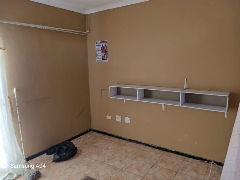 A small, empty room featuring tiled flooring, a wall-mounted storage shelf, and electrical power points.