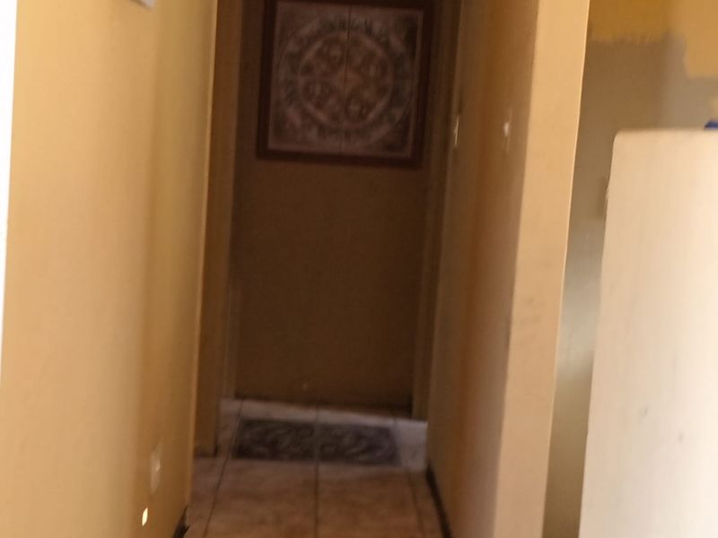 A narrow interior hallway featuring tiled flooring and neutral wall tones, providing access to adjacent rooms within the property.