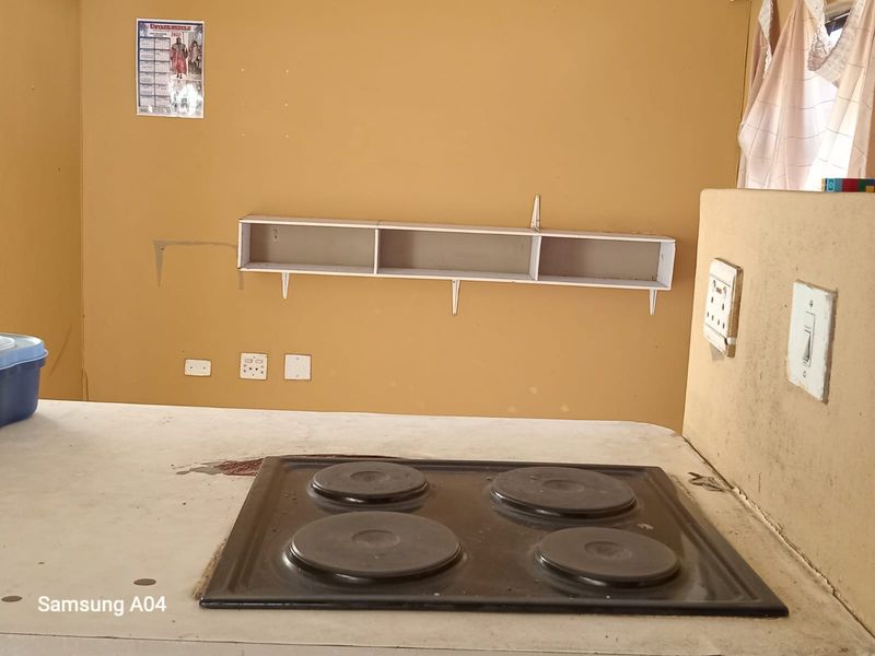 A functional kitchen area featuring a built-in four-plate electric hob, wall-mounted shelving, and basic electrical power points.