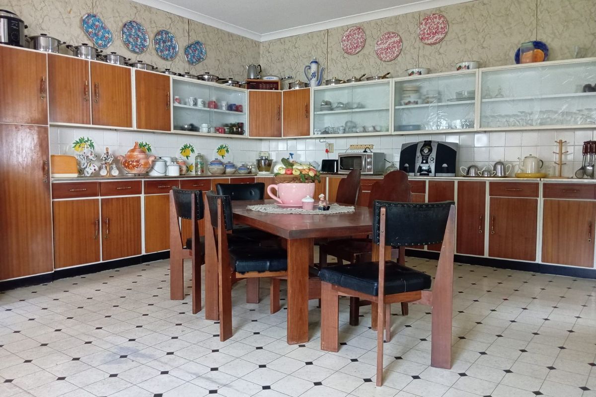 A spacious kitchen featuring extensive wooden cabinetry, tiled splashbacks, and a central dining area with classic patterned flooring.