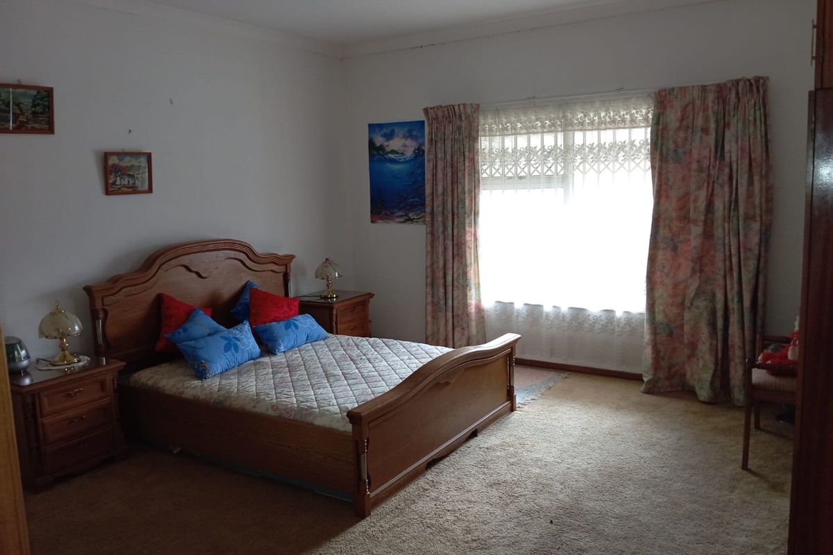 A spacious bedroom featuring neutral walls, carpeted flooring, and a large window with natural light.