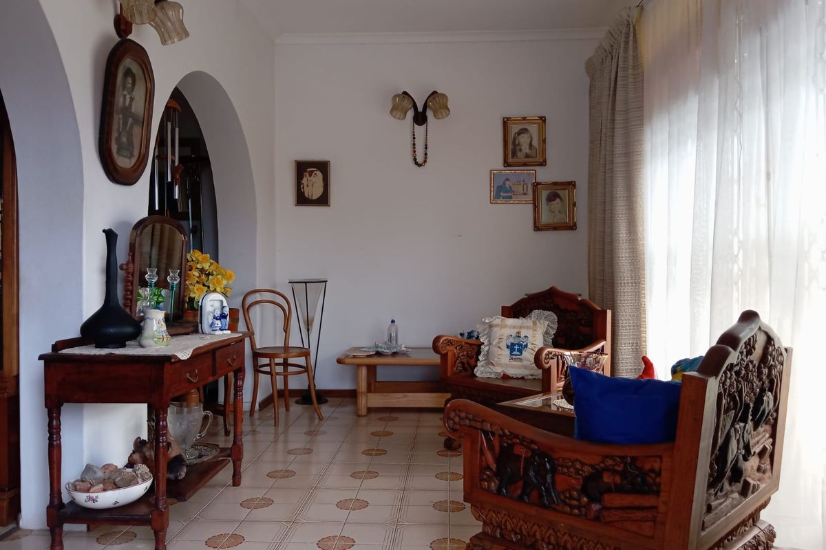 A living room featuring arched doorways, tiled flooring, and wall-mounted light fixtures, offering a traditional layout with natural light from the window.