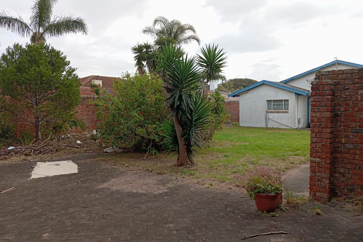 A rear garden area featuring a paved patio, lawn, and perimeter brick walls, requiring landscaping and maintenance to improve the outdoor space.
