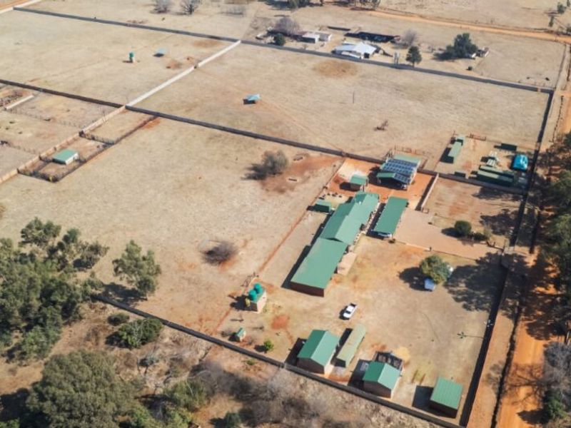 Aerial view of a large farm property featuring multiple outbuildings, fenced paddocks, solar panel installations, and water storage tanks.