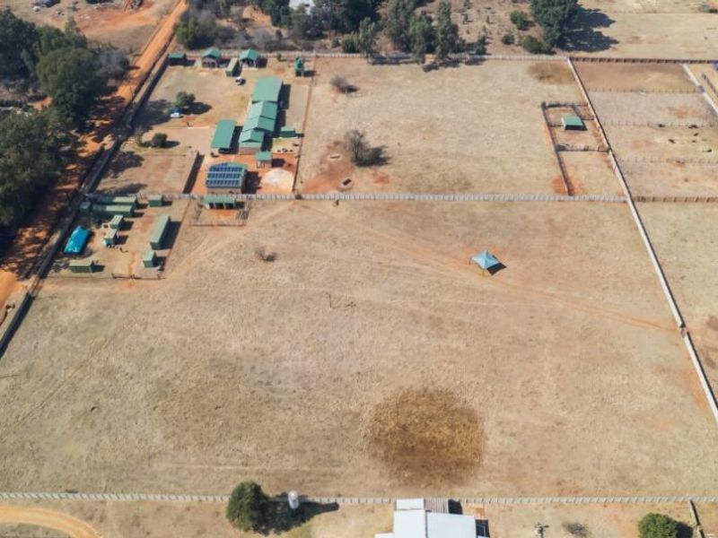 Aerial view of a large farm property featuring multiple outbuildings, fenced paddocks, solar panel installations, and water storage infrastructure.