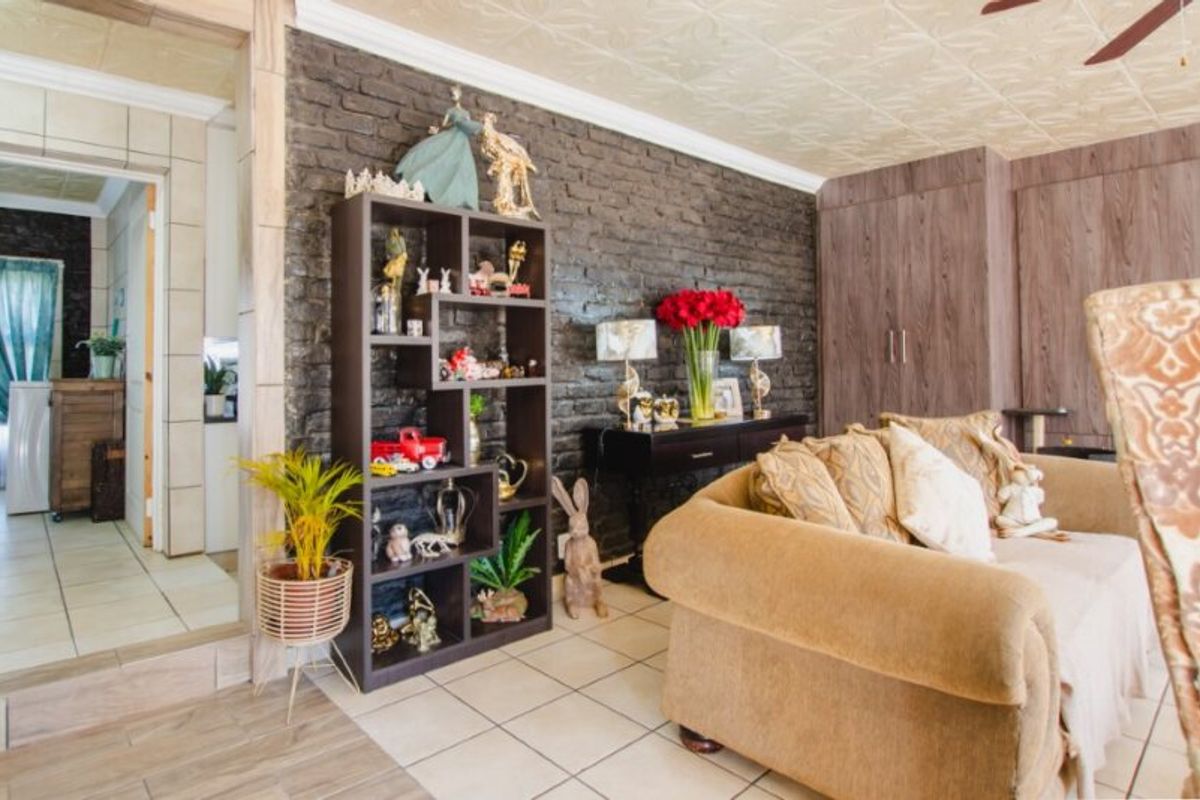Living room featuring an exposed dark brick feature wall, built-in storage cabinetry, tiled flooring, and decorative ceiling tiles.