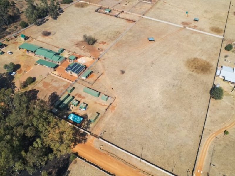 Aerial view of a large farm property featuring multiple outbuildings, fenced paddocks, solar panel installation, and a swimming pool.