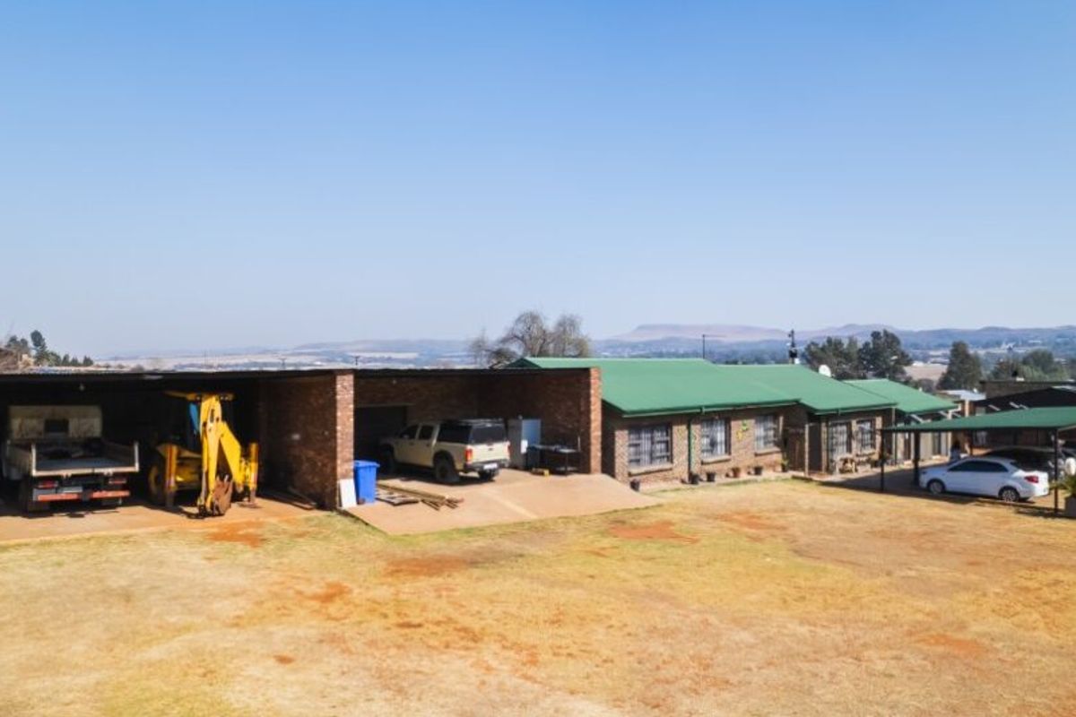 An aerial view of the farm property featuring a brick building with a green metal roof, extensive carport structures, and a large open yard area.