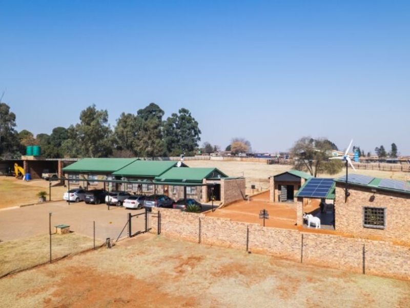 Aerial view of a farm property featuring multiple buildings, solar energy infrastructure, a wind turbine, paved driveway, and extensive surrounding land.