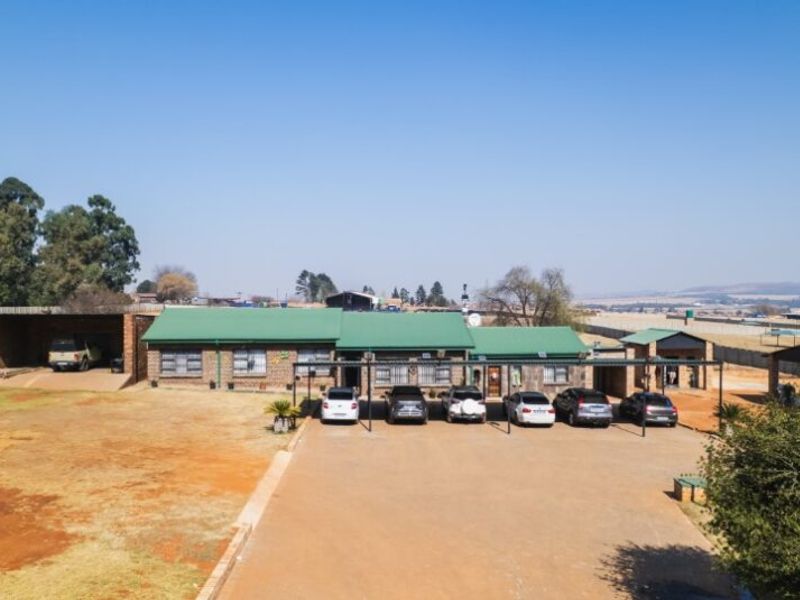 Aerial view of a farm property featuring a main residence with a metal roof, extensive driveway, and multiple carport structures.