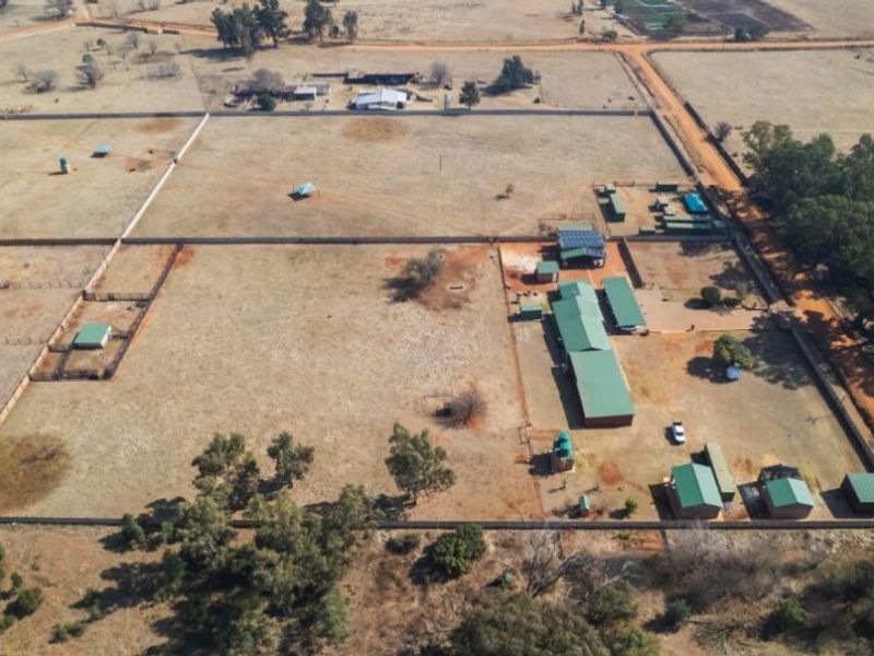 Aerial view of a farm property featuring multiple outbuildings, fenced paddocks, solar panel installations, and water storage tanks on a large rural plot.