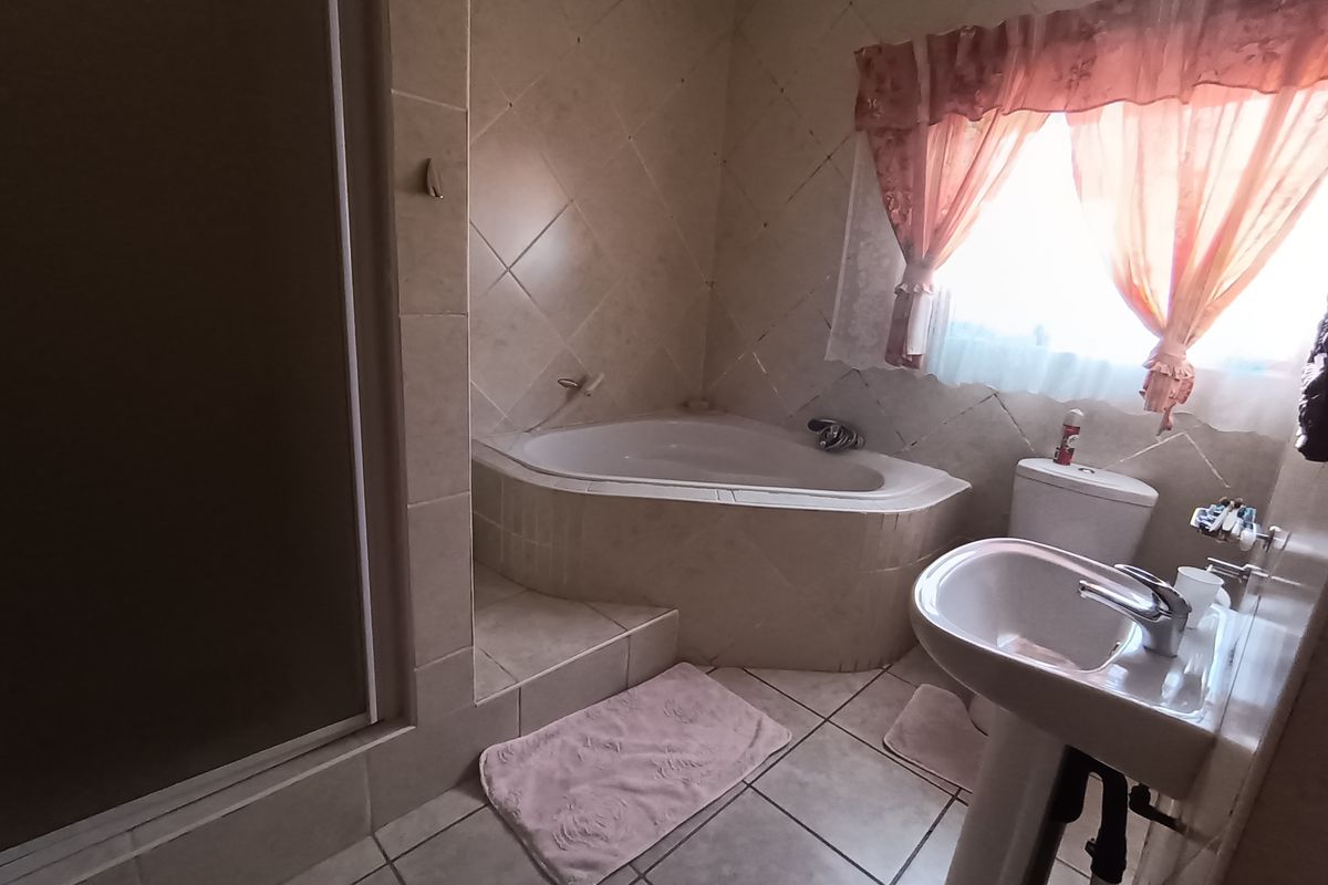A functional bathroom featuring a corner bathtub, pedestal basin, toilet, and a separate shower enclosure with neutral wall and floor tiling.